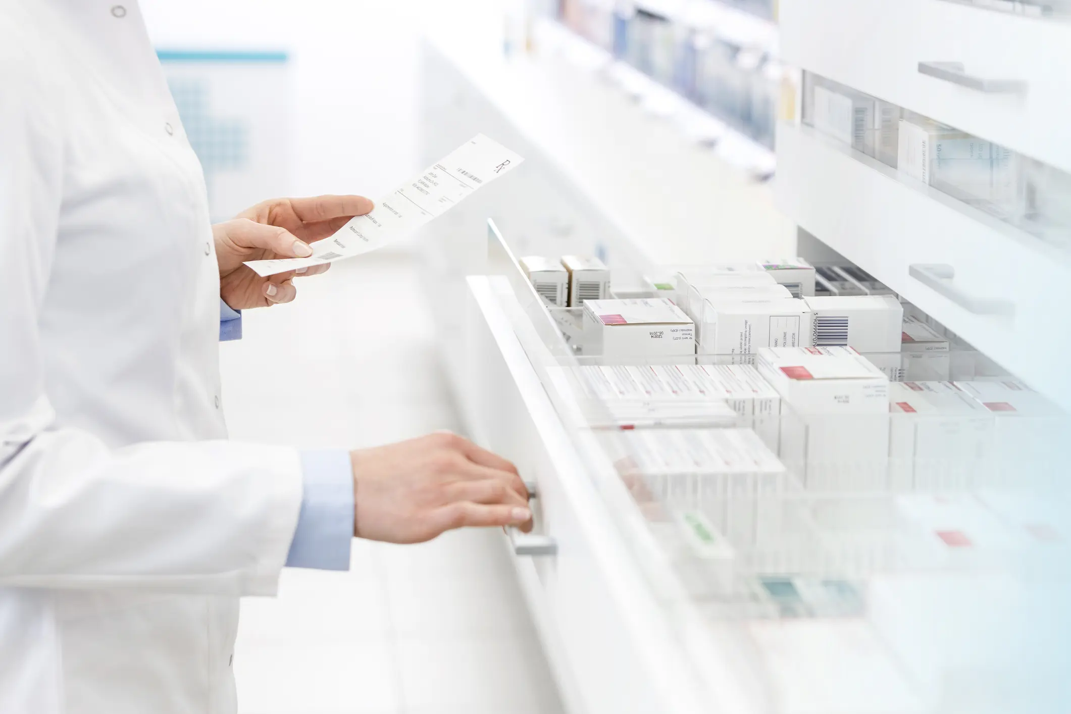 Pharmacist in a white coat checking a prescription slip and opening a drawer full of organized medication boxes in a bright pharmacy, illustrating personalized pharmacy services, prescription transfer, medication review, and refill assistance